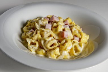 Beyaz arka planda kremalı ve jambonlu tortellini makarnasıyla çorba kasesi.