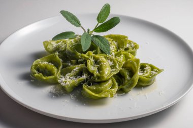 Beyaz arka planda yeşil ravioli, adaçayı ve parmesan peyniri.