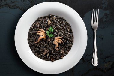 Kalamar mürekkebi ve çatalla koyu arkaplanda risotto tabağının üst görüntüsü