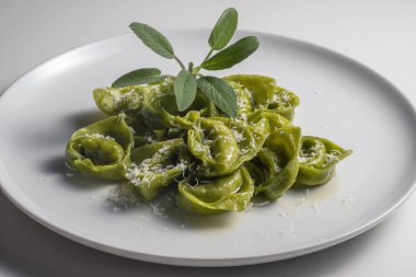 Beyaz arka planda yeşil ravioli, adaçayı ve parmesan peyniri.