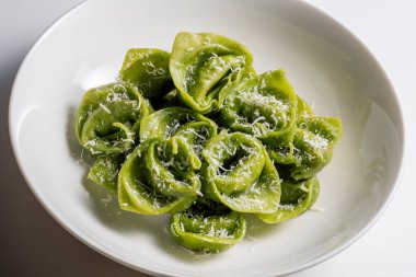 Beyaz arka planda parmesanlı yeşil ravioli kasesi.