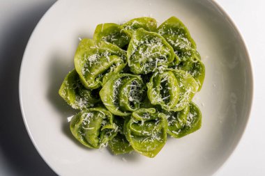 Beyaz arka planda parmesanlı yeşil ravioli kasesi.