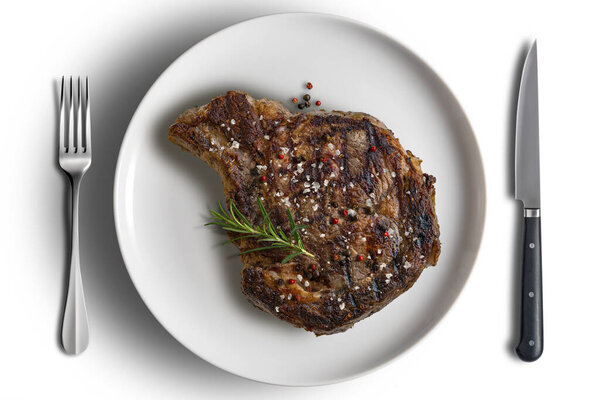 Top view of Flavored Whole rib eye beef on white round plate with cutlery isolated on white background
