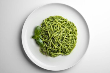 Beyaz tabağın üst görüntüsü beyaz arka planda fesleğen yapraklı Ceneviz pesto soslu linguine ile