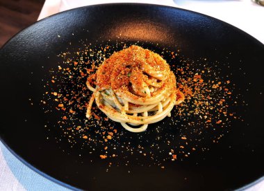 Siyah tabak, porsiyon spagetti, kızarmış ekmek kırıntıları ve rendelenmiş bottarga.