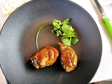 Top view of Black plate with portion of pork cheeks with green sauce snd salad clipart