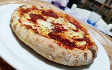 Tabak ve salamlı pizza. Yüksek kenarlı ve servis masasında.