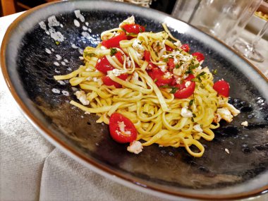 Yengeç etli ve domatesli siyah bir tabak Tagliolini makarna.