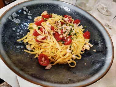 Yengeç etli ve domatesli siyah bir tabak Tagliolini makarna.