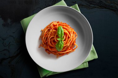 Beyaz kasenin üst görüntüsü domates soslu spagetti ve koyu arkaplanda izole edilmiş fesleğen.