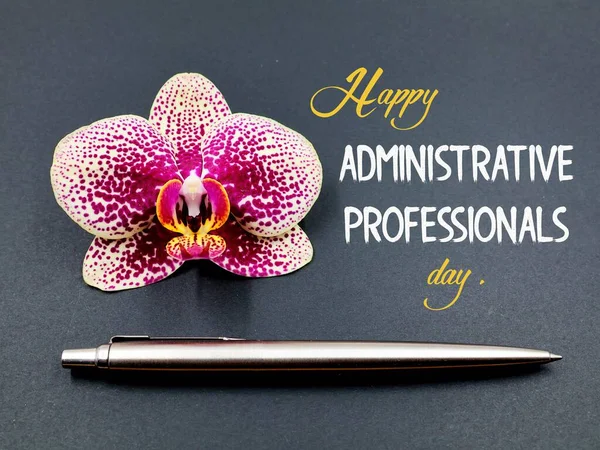 Orchid flower and pen isolated on black background . Text \'Happy administrative professionals day\' . Concept secretary day.