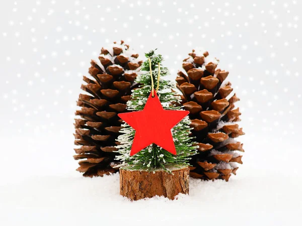 Kırmızı yıldızlı minyatür Noel ağacı ve karda iki kozalak. Noel Konsepti.