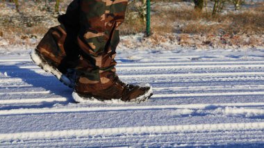 Karda yürüyorum. Yürüyüş botları ve kamuflaj pantolonu. Seçici odak.