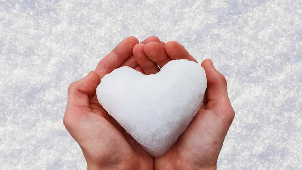 Heart of snow in two hands in front of a snowy background. Concept love, Valentine\'s day, wedding...Copy space.