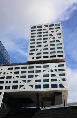 Modern , tall and white building with windows against a blue sky with white clouds. Modern architecture. clipart