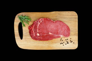 Tahta kesme tahtasındaki pirzola bifteği ve siyah arka planda biberiye ve karabiber. Lezzetli bir parça kırmızı et. Üst görünüm.