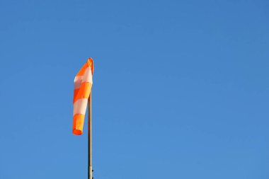 Mavi gökyüzünde turuncu ve beyaz çizgili yel çorabı. Uçak için sinyal. Rüzgâr soketi hala rüzgarın olmadığını gösteriyor..
