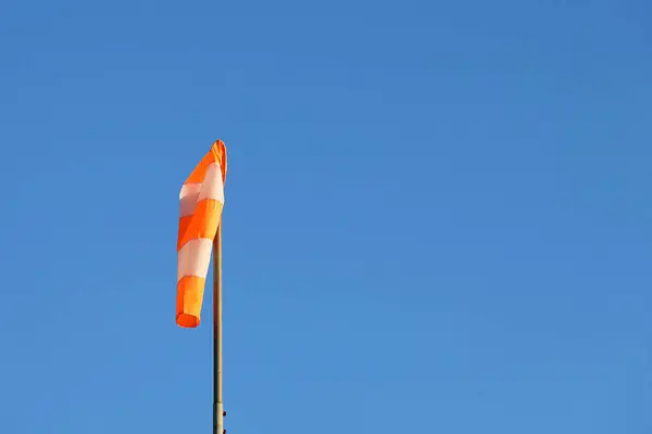Mavi gökyüzünde turuncu ve beyaz çizgili yel çorabı. Uçak için sinyal. Rüzgâr soketi hala rüzgarın olmadığını gösteriyor..