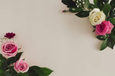 Taze pembe ve beyaz güller ve kumlu şeftali rengi pastel arka planda doğal yeşil yapraklarla yapılmış bir çiçek çerçevesi. Minimum düzlük.