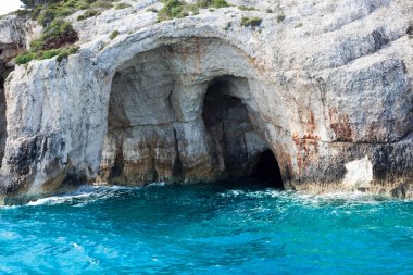 Mavi gökyüzü, dağları, kayaları, denizi ve turkuaz suyu olan kayalık sahil Yunanistan 'daki Zakynthos Adası' nın arka planında.