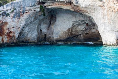 Mavi gökyüzü, dağları, kayaları, denizi ve turkuaz suyu olan kayalık sahil Yunanistan 'daki Zakynthos Adası' nın arka planında.