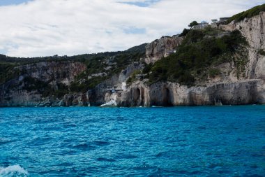 Mavi gökyüzü, dağları, kayaları, denizi ve turkuaz suyu olan kayalık sahil Yunanistan 'daki Zakynthos Adası' nın arka planında.