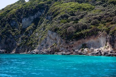 Mavi gökyüzü, dağları, kayaları, denizi ve turkuaz suyu olan kayalık sahil Yunanistan 'daki Zakynthos Adası' nın arka planında.