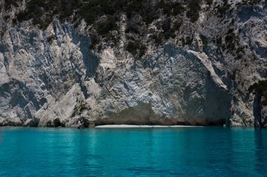 Mavi gökyüzü, dağları, kayaları, denizi ve turkuaz suyu olan kayalık sahil Yunanistan 'daki Zakynthos Adası' nın arka planında.