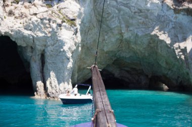 Mavi gökyüzü, dağları, kayaları, denizi ve turkuaz suyu olan kayalık sahil Yunanistan 'daki Zakynthos Adası' nın arka planında.