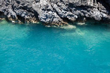 Mavi gökyüzü, dağları, kayaları, denizi ve turkuaz suyu olan kayalık sahil Yunanistan 'daki Zakynthos Adası' nın arka planında.