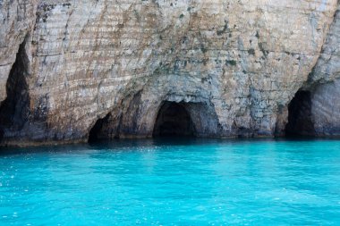 Mavi gökyüzü, dağları, kayaları, denizi ve turkuaz suyu olan kayalık sahil Yunanistan 'daki Zakynthos Adası' nın arka planında.