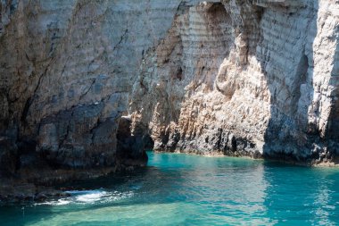 Mavi gökyüzü, dağları, kayaları, denizi ve turkuaz suyu olan kayalık sahil Yunanistan 'daki Zakynthos Adası' nın arka planında.