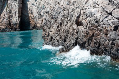 Mavi gökyüzü, dağları, kayaları, denizi ve turkuaz suyu olan kayalık sahil Yunanistan 'daki Zakynthos Adası' nın arka planında.