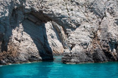 Mavi gökyüzü, dağları, kayaları, denizi ve turkuaz suyu olan kayalık sahil Yunanistan 'daki Zakynthos Adası' nın arka planında.