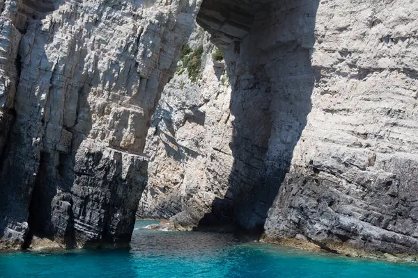 Mavi gökyüzü, dağları, kayaları, denizi ve turkuaz suyu olan kayalık sahil Yunanistan 'daki Zakynthos Adası' nın arka planında.