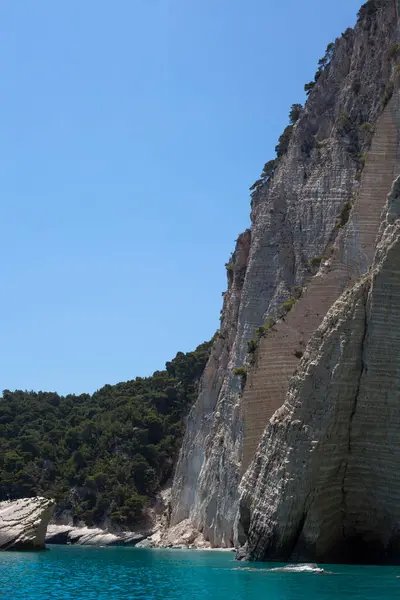 Mavi gökyüzü, dağları, kayaları, denizi ve turkuaz suyu olan kayalık sahil Yunanistan 'daki Zakynthos Adası' nın arka planında.