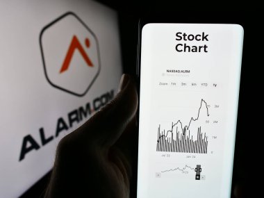 Stuttgart, Almanya - 04-29-2024: İş logosu önünde ABD 'li güvenlik şirketi Alarm.com Inc.' nin web sitesi ile cep telefonu bulunduran kişi. Telefon ekranının merkezine odaklan.