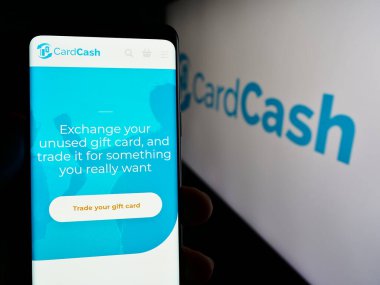 Stuttgart, Almanya - 04-29-2024: ABD 'li hediye kartı pazar yeri şirketi CardCash' in web sayfası ile logo önünde cep telefonu tutan kişi. Telefon ekranının merkezine odaklan.