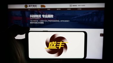 Stuttgart, Almanya - 04-29-2024: Çinli lojistik şirketi Shengfeng Development Ltd. 'nin logosuyla cep telefonu tutan kişi iş sayfasının önünde. Telefon ekranına odaklan.