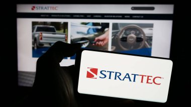 Stuttgart, Almanya - 05-02-2024: Amerikan otomotiv şirketi Strattec Security Corporation 'ın logosuna sahip cep telefonu sahibi kişi web sayfasının önünde. Telefon ekranına odaklan.
