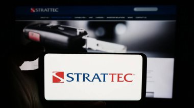 Stuttgart, Almanya - 05-02-2024: ABD 'li otomotiv şirketi Strattec Security Corporation' ın logosuyla cep telefonu sahibi kişi iş sayfası önünde. Telefon ekranına odaklan.