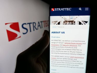 Stuttgart, Almanya - 05-02-2024: ABD 'li otomotiv şirketi Strattec Security Corporation' ın web sayfası ile logo önünde cep telefonu tutan kişi. Telefon ekranının merkezine odaklan.