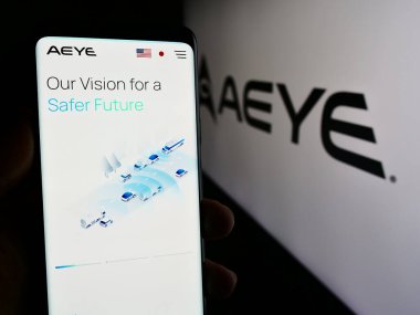 Stuttgart, Germany - 05-02-2024: Person holding smartphone with webpage of US lidar software company AEye Inc. in front of business logo. Focus on center of phone display. clipart