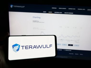 Stuttgart, Germany - 05-02-2024: Person holding mobile phone with logo of American Bitcoin mining company TeraWulf Inc. in front of business web page. Focus on phone display. clipart