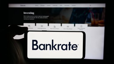 Stuttgart, Almanya - 05-03-2024: ABD 'li tüketici finans şirketi Bankrate LLC' nin logosuyla cep telefonu sahibi kişi iş sayfası önünde. Telefon ekranına odaklan.