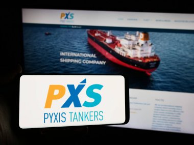 Stuttgart, Germany - 05-03-2024: Person holding smartphone with logo of Greek shipping company Pyxis Tankers Inc. (PXS) in front of website. Focus on phone display. clipart