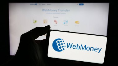Stuttgart, Almanya - 05-03-2024: Rus çevrimiçi ödeme şirketi WebMoney Transfer 'in logosuna sahip cep telefonu sahibi kişi iş sayfasının önünde. Telefon ekranına odaklan.