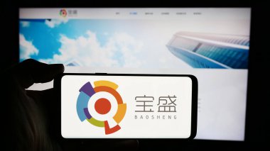 Stuttgart, Almanya - 05-03-2024: Çinli şirket Baosheng Media Group Holding Limited 'in logosuna sahip cep telefonu sahibi kişi iş sayfası önünde bulunuyor. Telefon ekranına odaklan.