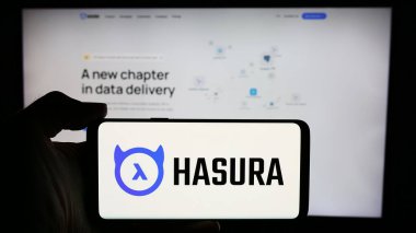 Stuttgart, Almanya - 05-07-2024: Amerikan yazılım geliştirme şirketi Hasura Inc. 'nin logosuyla cep telefonu sahibi kişi iş sayfasının önünde. Telefon ekranına odaklan.