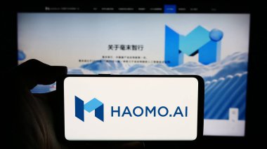 Stuttgart, Almanya - 05-08-2024: Çinli otonom sürücü şirketi Haomo.I 'nin logosuyla cep telefonu tutan kişi iş sayfasının önünde. Telefon ekranına odaklan.